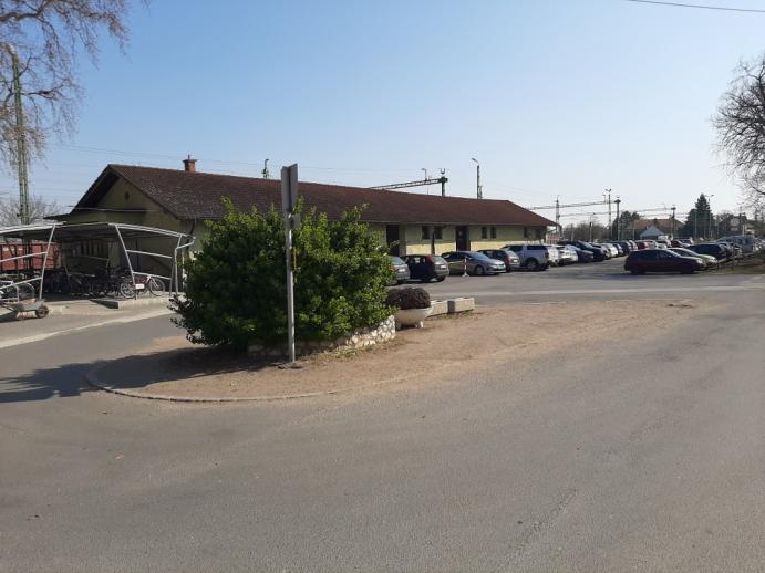 Fertőszentmiklós állomás előtti parkoló és közlekedési csomópont, személygépkocsikkal és zöld szigettel a tér közepén.